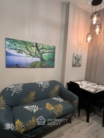 Cozy living room with stylish sofa and elegant dining area, featuring modern lighting and nature-themed artwork.