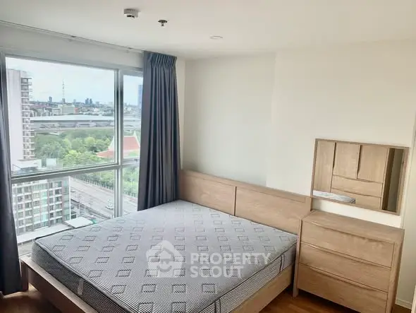 Modern bedroom with city view, featuring a wooden bed and dresser, large window with curtains.