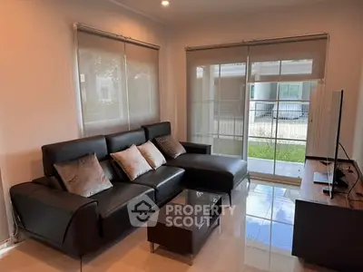 Modern living room with sleek black leather sofa and large windows for natural light.