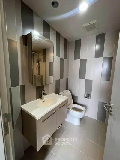 Modern bathroom with sleek design and stylish tiles, featuring a contemporary sink and toilet.