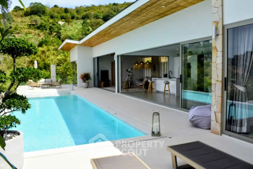 Luxurious modern villa with infinity pool and open-plan kitchen, surrounded by lush greenery.