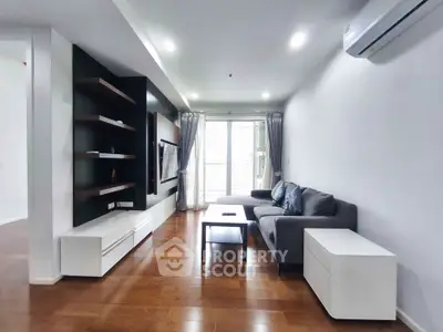 Modern living room with sleek furniture and hardwood floors, featuring a cozy gray sofa and wall-mounted TV.