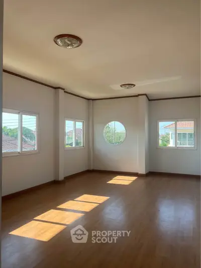 Spacious sunlit room with unique circular window and wooden flooring