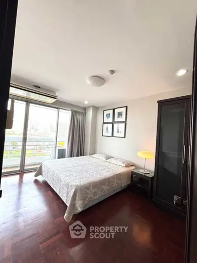 Spacious bedroom with large window and city view, featuring elegant wooden flooring and modern decor.