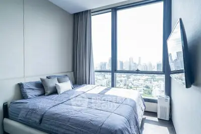 Modern bedroom with city view and large windows, featuring a stylish bed and wall-mounted TV.