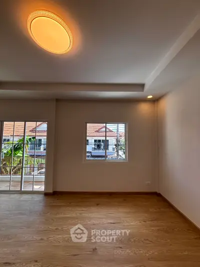 Spacious empty room with wooden flooring and large windows offering natural light and balcony access.