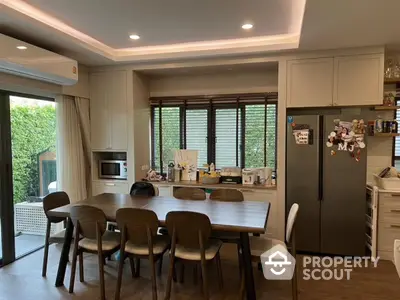 Modern kitchen with dining area, featuring sleek cabinets and large windows for natural light.