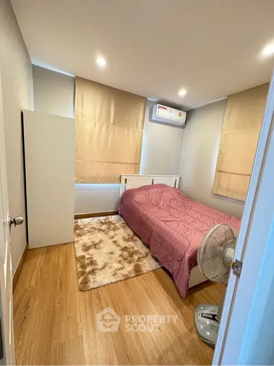 Cozy bedroom with wooden flooring, single bed, and air conditioning in a modern apartment.