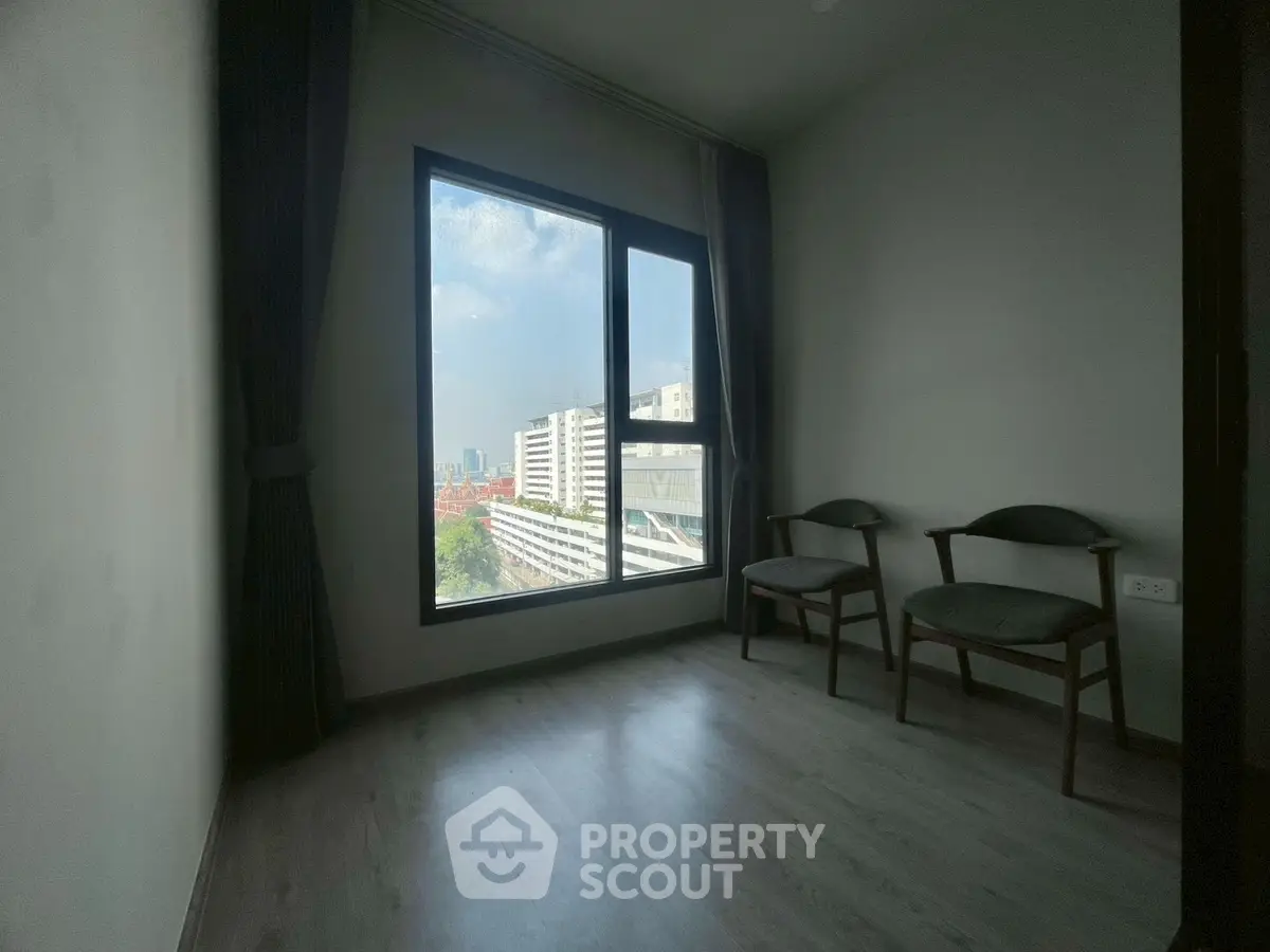 Minimalist room with large window offering city view, featuring two chairs and wooden flooring.