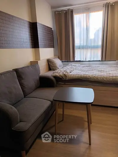 Cozy studio apartment with modern decor, featuring a comfortable sofa and bed near a sunlit window.