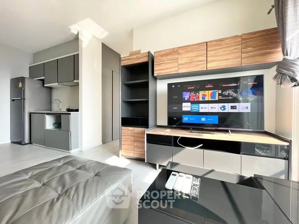 Modern living room with sleek furniture and open kitchen layout, featuring a smart TV and ample natural light.