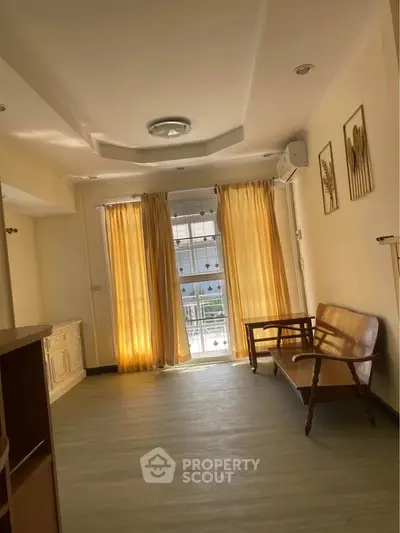 Bright living room with wooden flooring and elegant curtains, featuring a classic wooden bench and wall art.