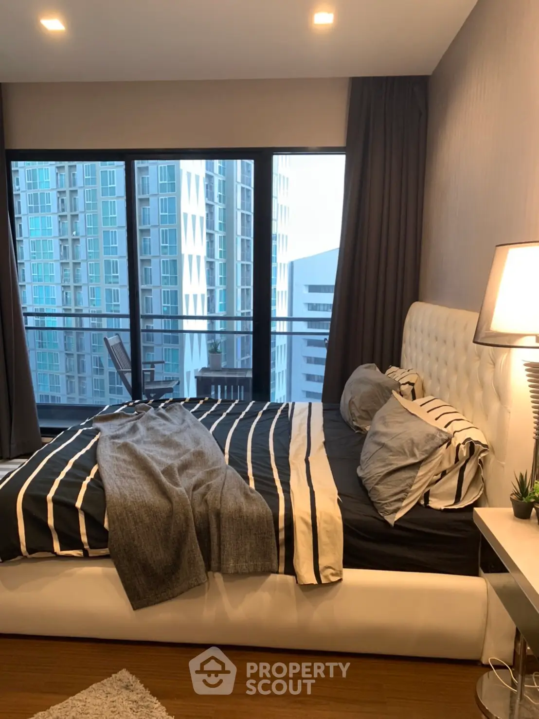 Modern bedroom with city view, featuring stylish decor and large windows for natural light.