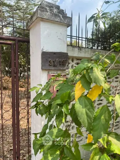Charming entrance gate with lush greenery and rustic appeal, perfect for a serene property setting.