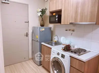 Modern compact kitchen with wooden cabinets, washing machine, and sleek appliances in cozy apartment.