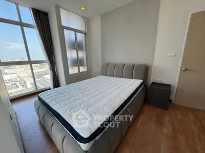 Modern bedroom with large windows and city view, featuring a stylish bed and wooden flooring.