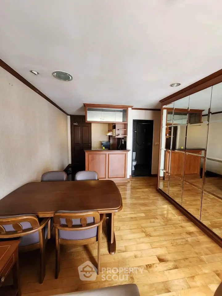 Spacious dining area with wooden flooring and mirrored wall in modern apartment.