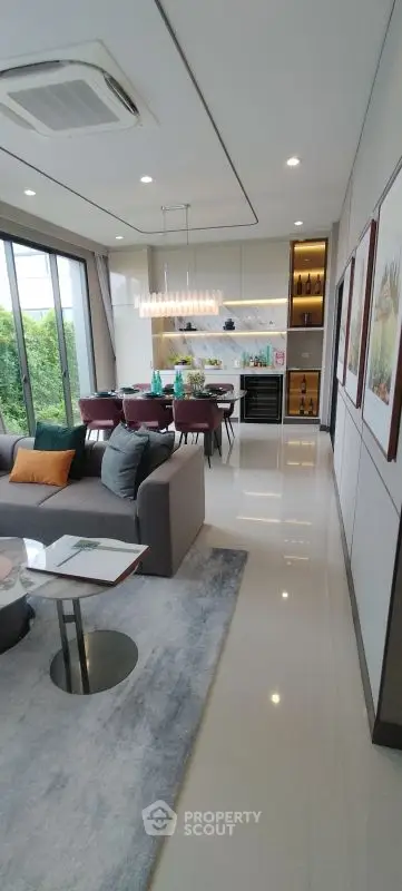 Modern open-layout living room with dining area, sleek furniture, and large windows overlooking greenery.