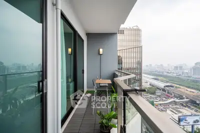 Modern balcony with city view, glass railing, and outdoor seating in high-rise apartment.
