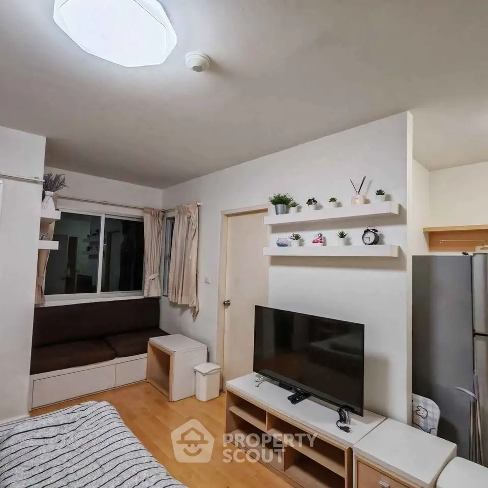 Cozy living room with modern decor and natural light, featuring a TV and stylish shelving.