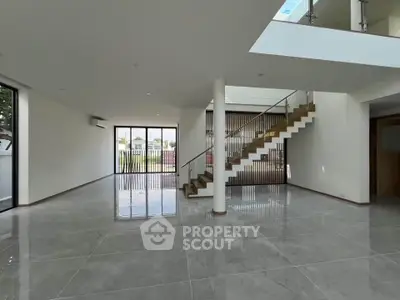 Spacious modern living room with sleek staircase and large windows offering abundant natural light.