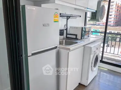 Modern kitchen with appliances including fridge, microwave, and washing machine in a bright apartment.