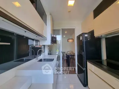 Modern kitchen with sleek cabinetry and black appliances, featuring a view into a stylish dining area.
