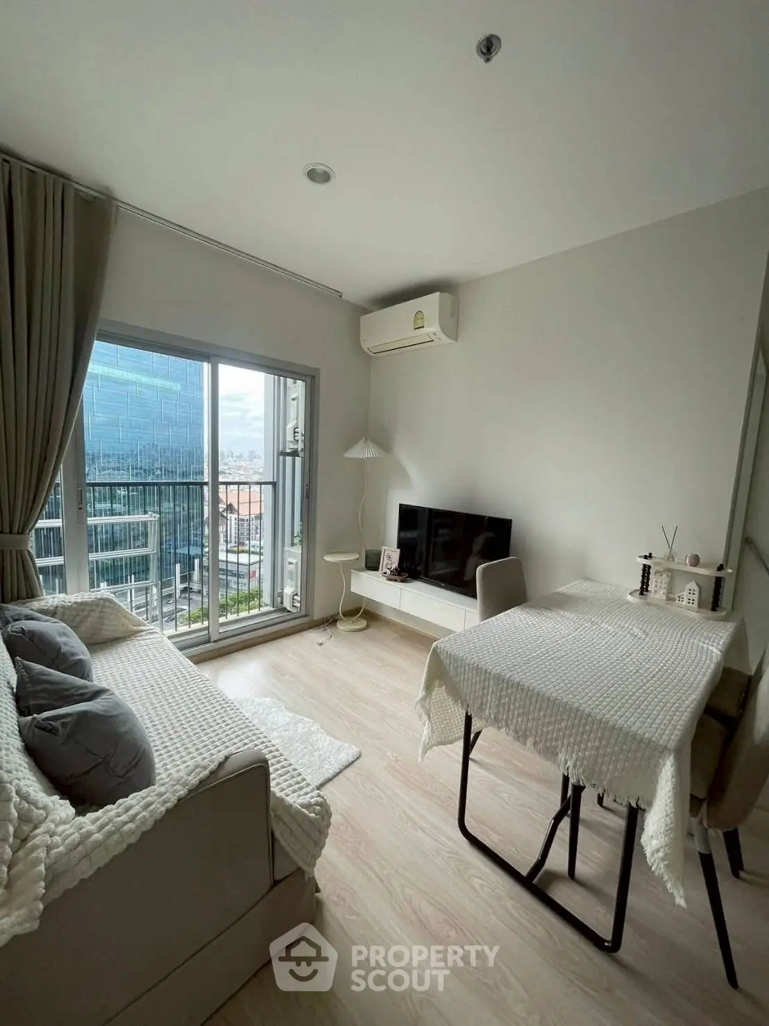 Modern living room with large window and city view, featuring cozy sofa and dining area.