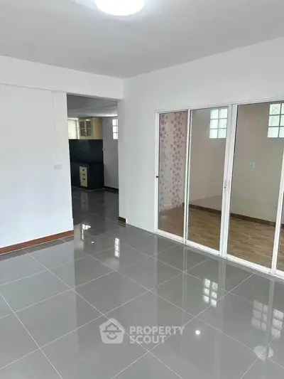 Spacious modern living room with sleek tile flooring and sliding glass doors leading to a cozy kitchen.