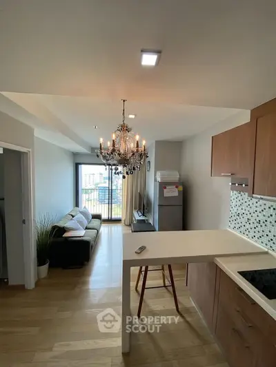 Modern open-plan kitchen and living room with chandelier and balcony view.