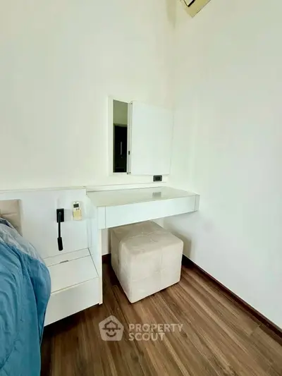 Modern bedroom with sleek white furniture and wooden flooring, featuring a stylish vanity area.