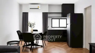 Modern open-layout kitchen and dining area with sleek black furniture and wooden flooring.