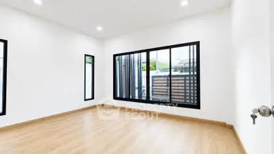 Spacious empty room with large windows and wooden flooring, perfect for customization.