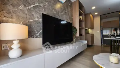 Modern living room with stylish decor and large TV, open kitchen layout.