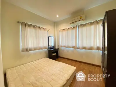 Cozy bedroom with natural light, wooden flooring, and air conditioning in modern apartment.