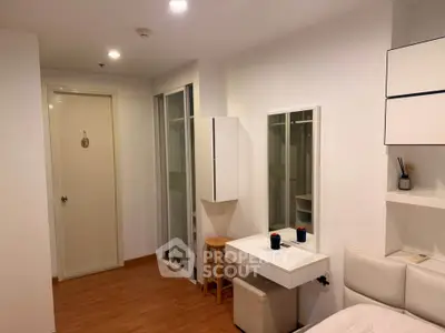 Modern bedroom with sleek white furniture and wooden flooring, featuring a vanity and closet space.