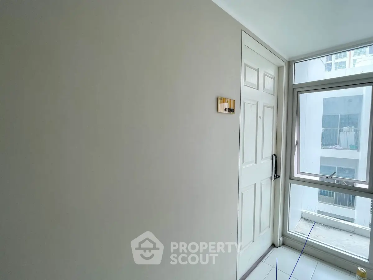Modern apartment entrance with white door and large window offering natural light.