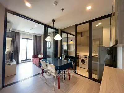 Modern open-plan living room with dining area and kitchen featuring washing machine and stylish lighting.