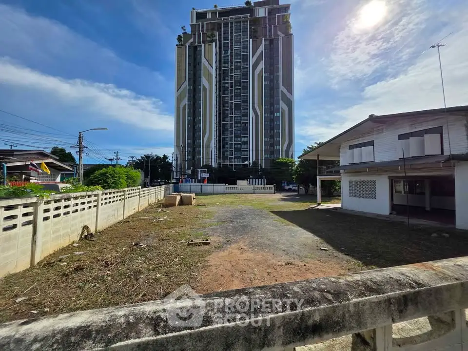 Modern high-rise building with adjacent vacant lot under a clear blue sky.