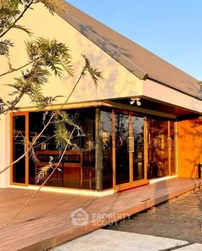 Modern home with large glass doors and wooden deck in sunset light.
