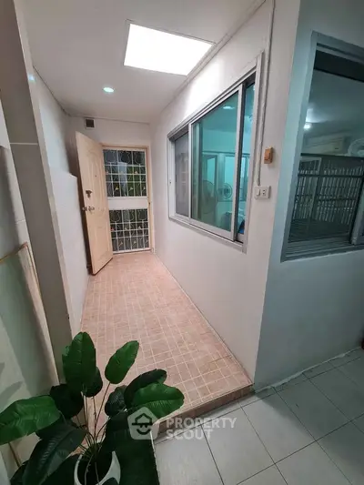 Bright hallway with tiled floor and large window, leading to a door with natural light.