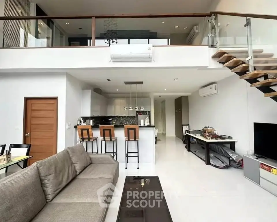 Spacious modern living room with open kitchen and mezzanine, featuring sleek design and ample natural light.