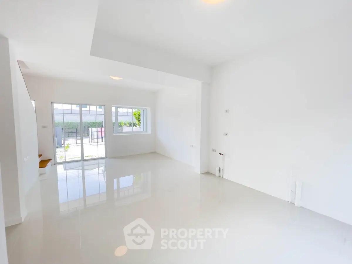 Spacious and bright empty living room with large windows and glossy white floors.