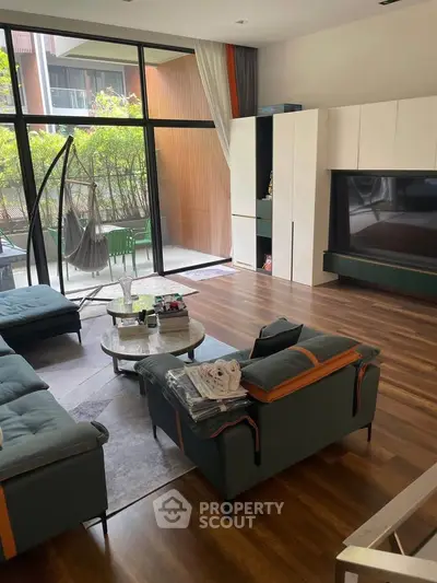 Spacious modern living room with large windows and stylish furniture, overlooking a private garden area.