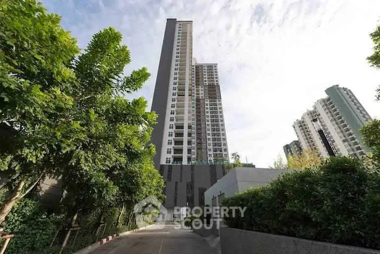Modern high-rise building with lush greenery and clear sky view.