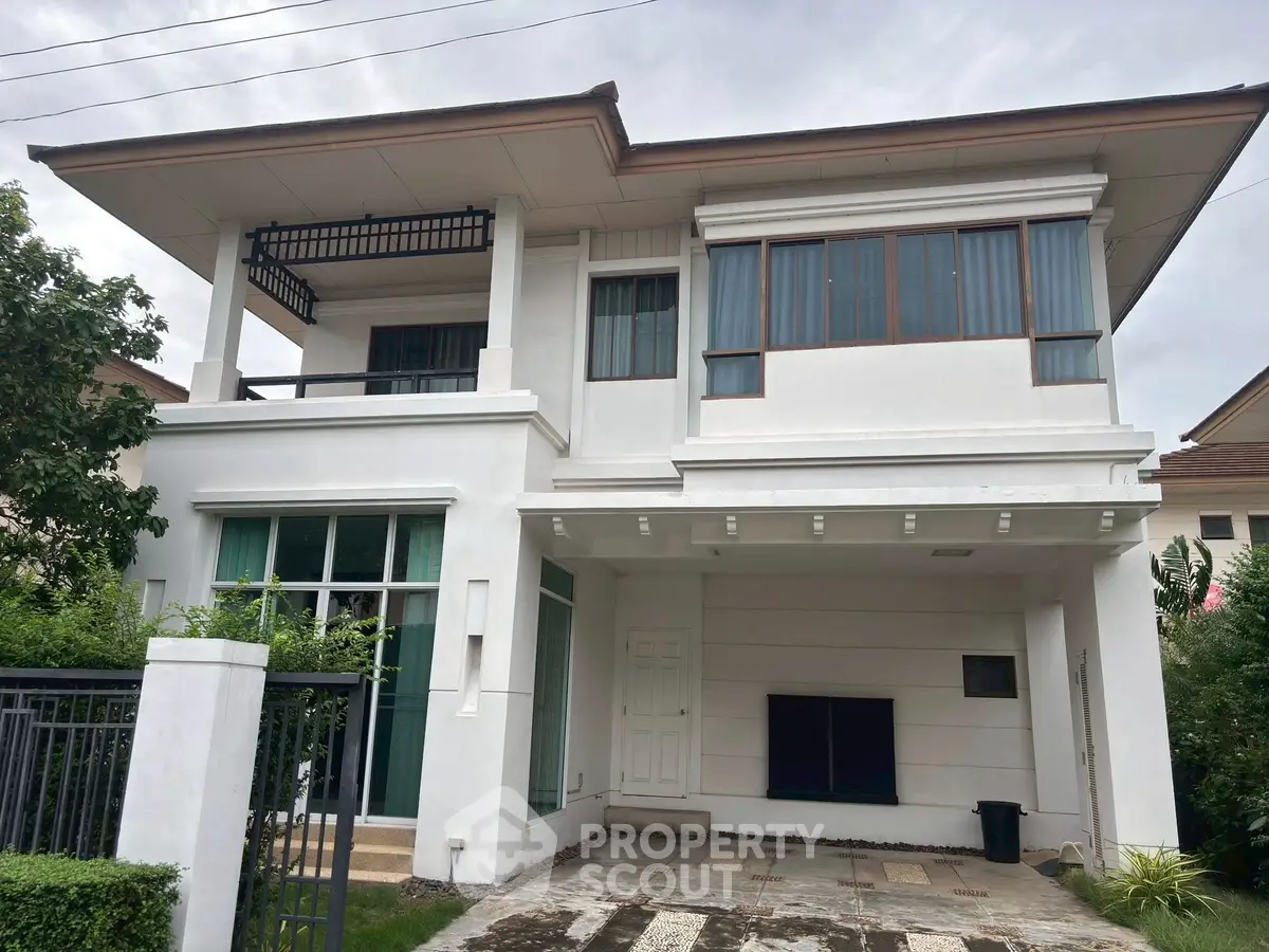 Elegant two-story white house with modern design and large windows, featuring a spacious balcony and lush greenery.