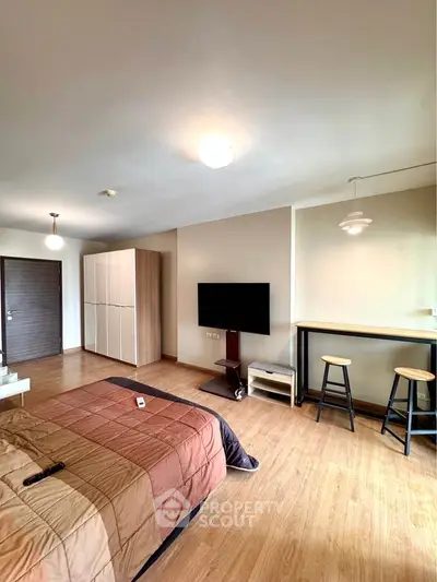Spacious modern bedroom with TV and seating area, featuring stylish wooden flooring.