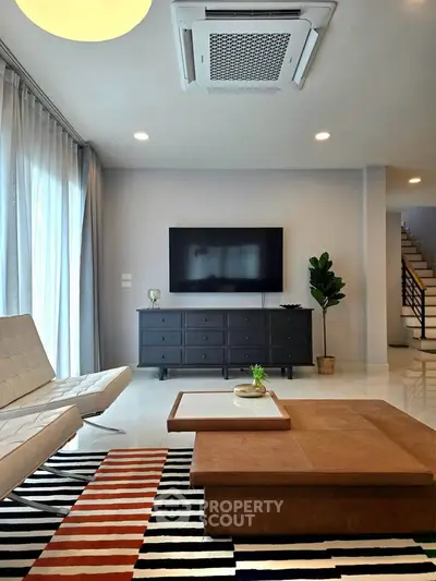 Modern living room with stylish furniture and wall-mounted TV, featuring a chic rug and natural light.