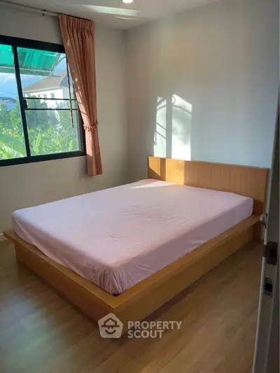 Cozy bedroom with natural light and wooden flooring, perfect for relaxation.