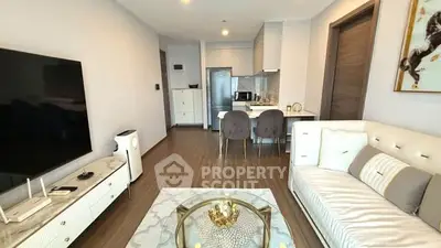 Modern living room with elegant decor and open kitchen layout, featuring a cozy sofa and large TV.